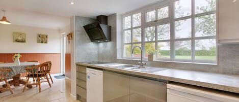 A modern kitchen with a large window, a dishwasher, and a dining area with wooden chairs and a table.