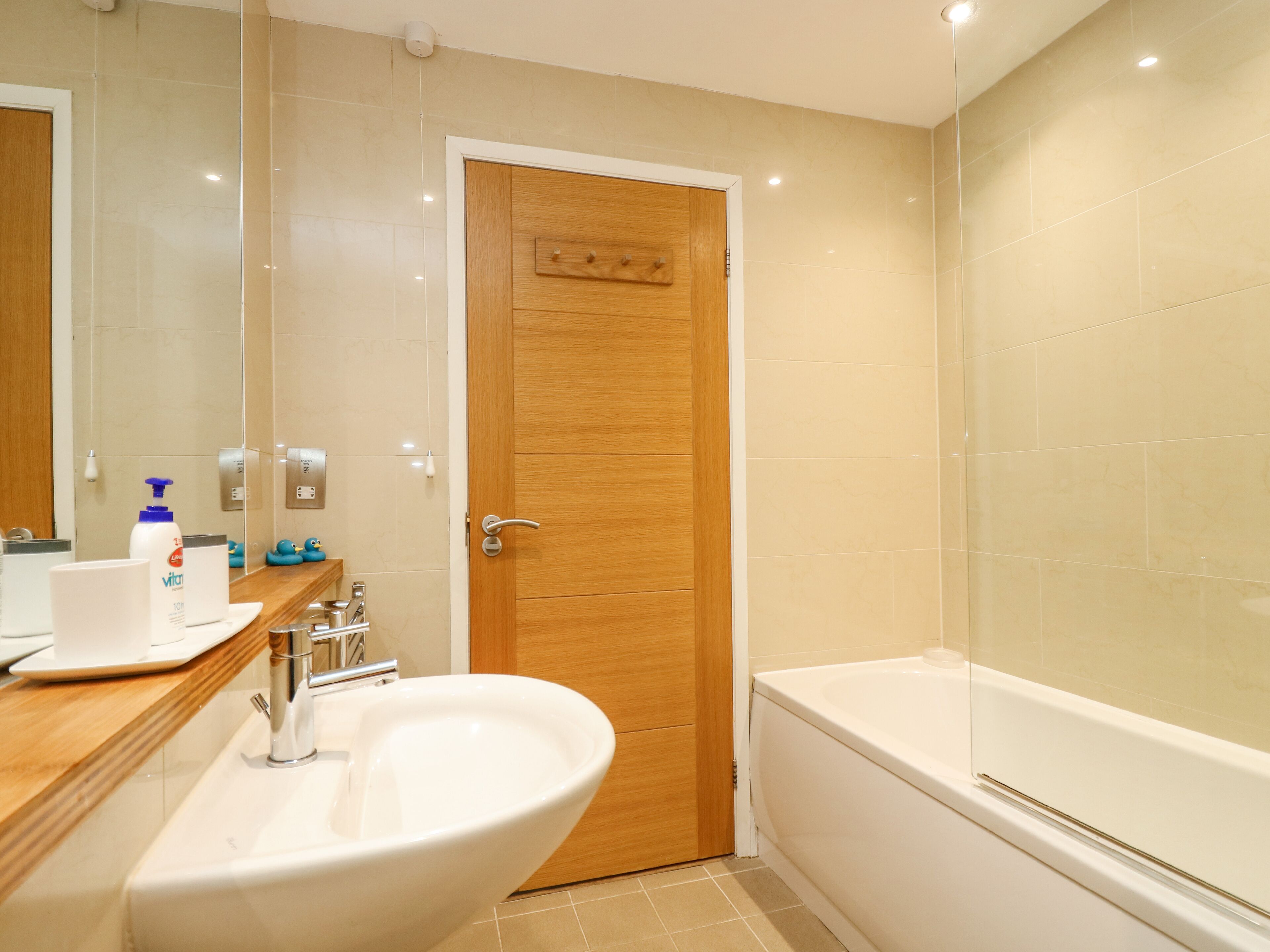 A modern bathroom with a wooden door, a sink, a mirror, and a bathtub.