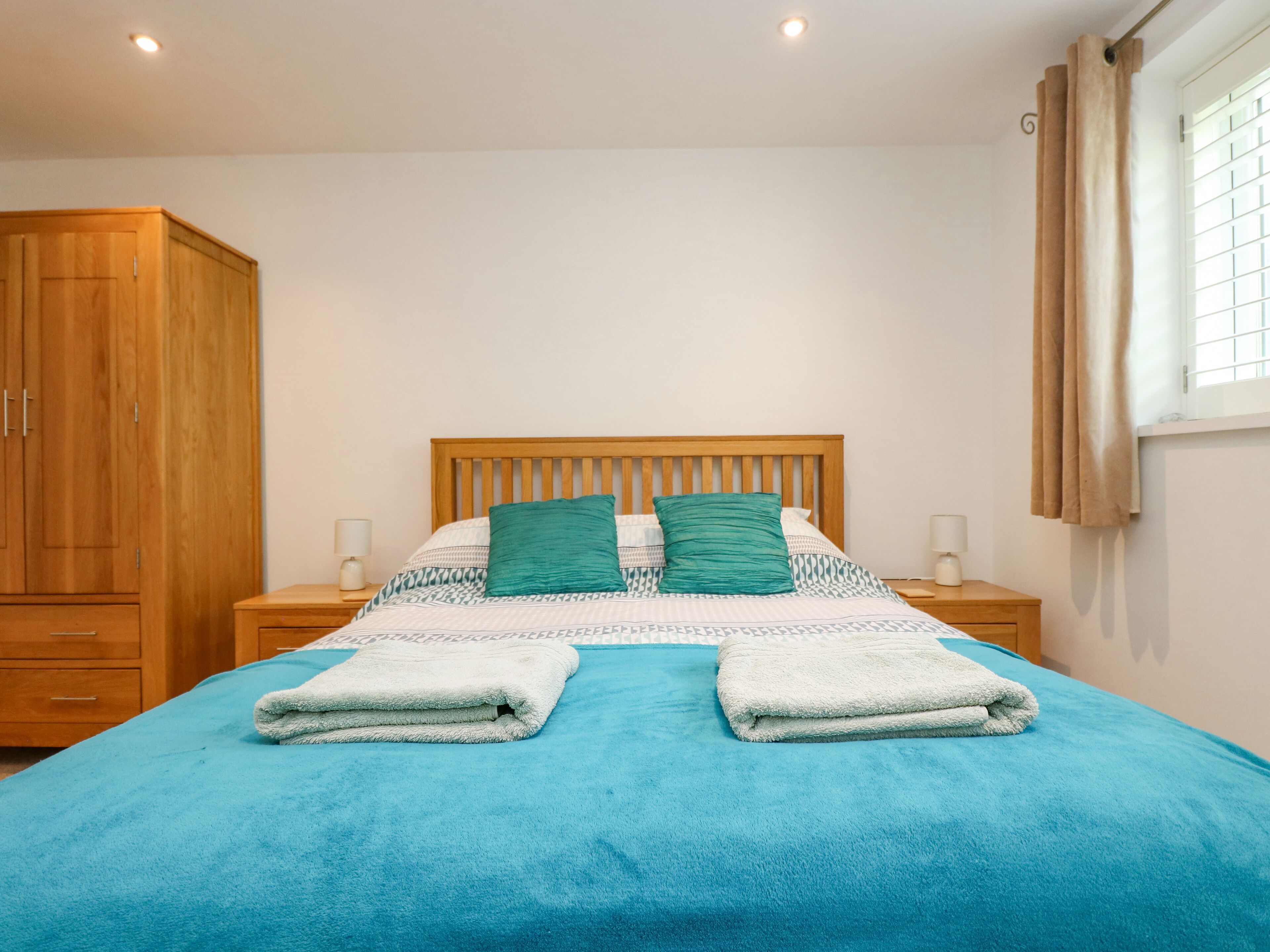 Une chambre à coucher avec une tête de lit en bois, deux coussins verts, une couvre-lit bleue et une pile de serviettes pliées.