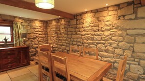 A dining area with a wooden table and chairs, a stone wall, and a wooden cabinet. - Usherwoods Barn (Lancaster)