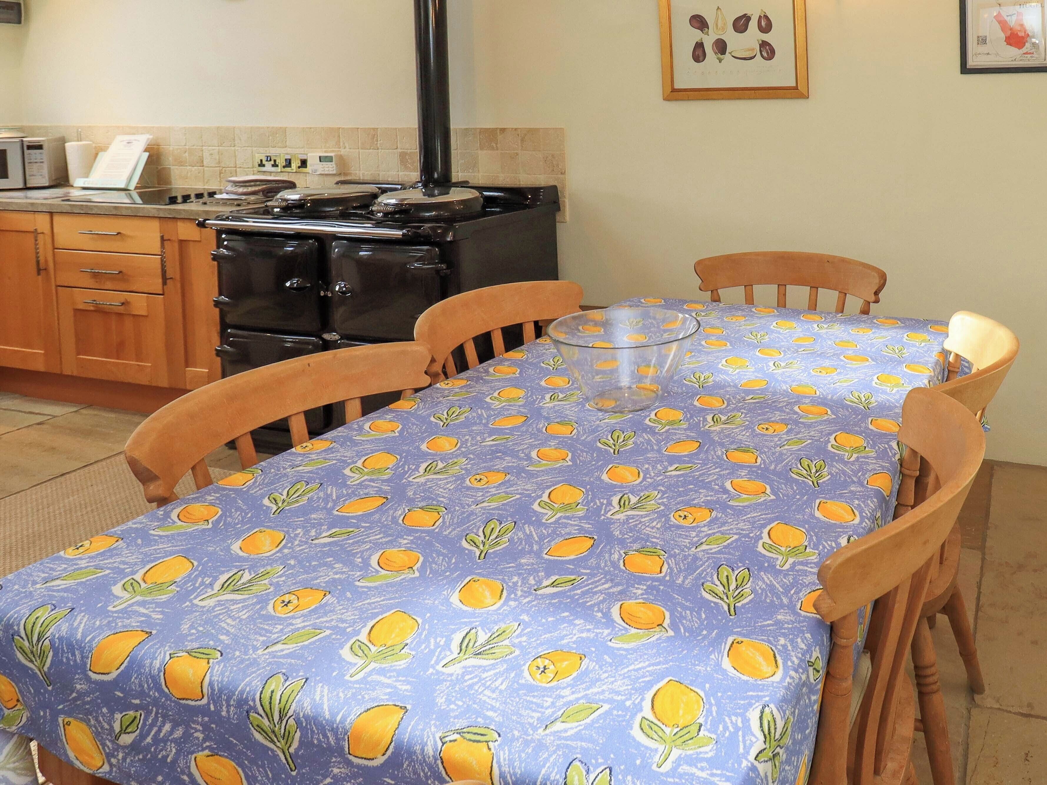 Een keuken met houten kasten, een fornuis en een eettafel met een tafelkleed met citroenmotief.
