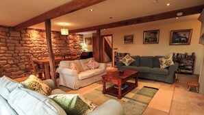 A cozy living room with a stone wall, a wooden ceiling, and a fireplace. There are two sofas and a coffee table. - Usherwoods Barn (Lancaster)
