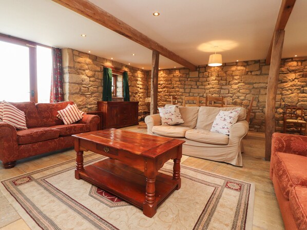 Cozy living room with a stone wall backdrop, wooden beams, and comfortable seating areas.