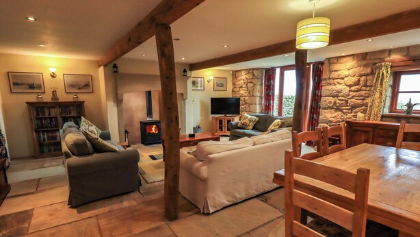 A cozy living room with a stone fireplace, wooden furniture, and a television. - Usherwoods Barn (Lancaster)