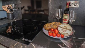 Une cuisine équipée d’une plaque de cuisson à induction Bosch, une assiette de pain accompagnée de tomates cerises, une bouteille de vin Le Rustique et deux verres.