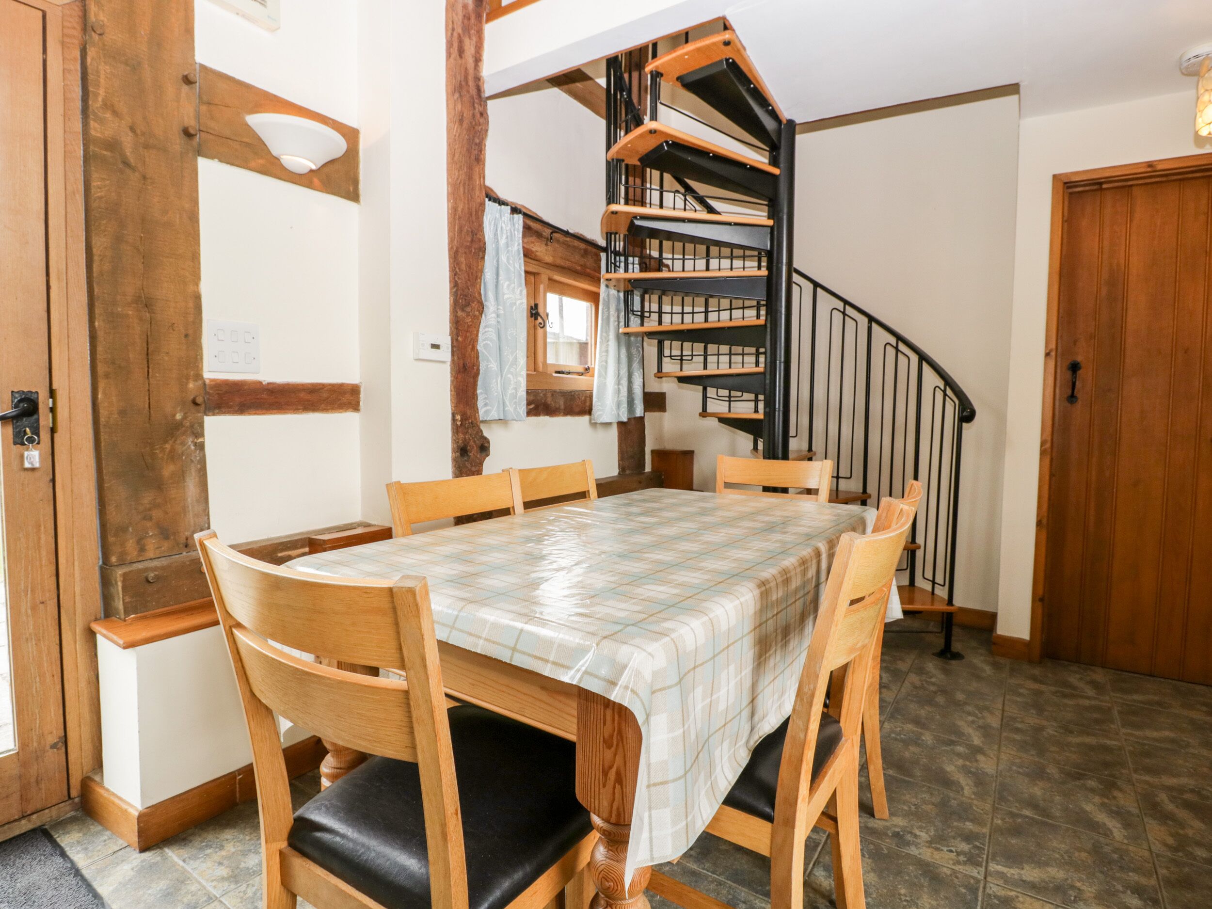 A dining area with a wooden table and chairs, a spiral staircase, and a wooden door.