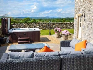 A patio with a hot tub, wicker furniture, and a stone wall backdrop. - Ox Hey Barn (Clitheroe)