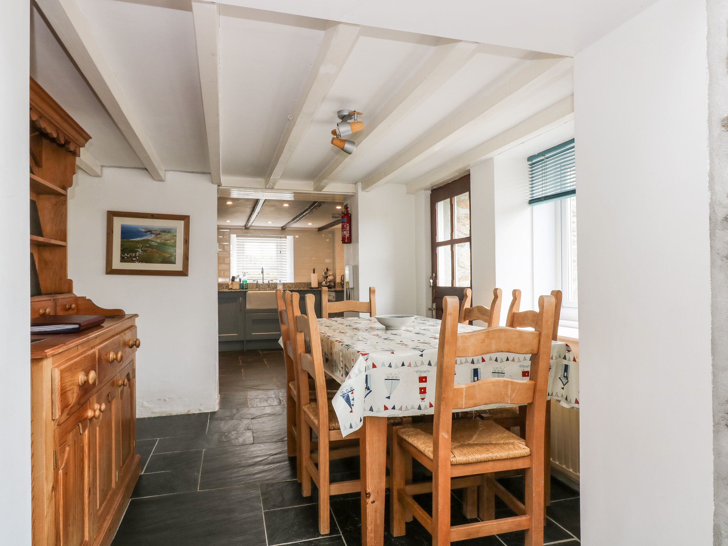 Zona pranzo con tavolo apparecchiato per quattro, sedie in legno, un armadietto in legno e una cucina sullo sfondo.