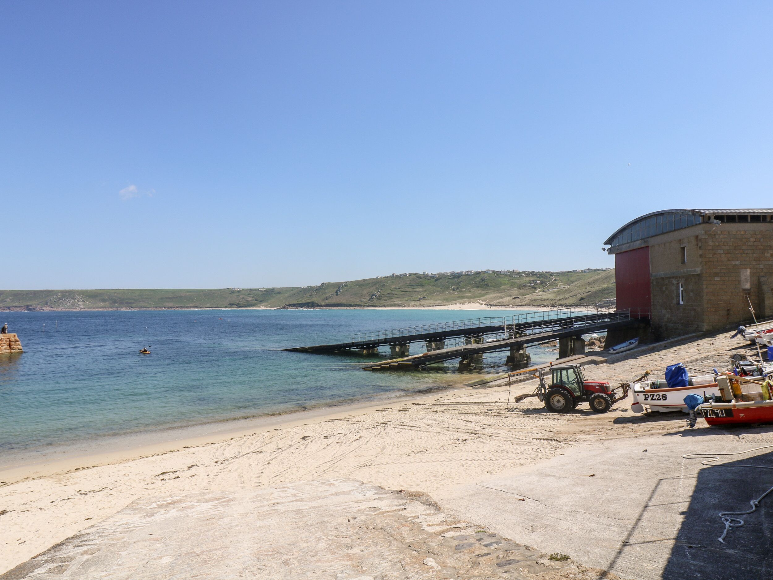 Eine Küstenlandschaft mit Sandstrand, einer Anlegestelle und einem Gebäude mit roter Tür.