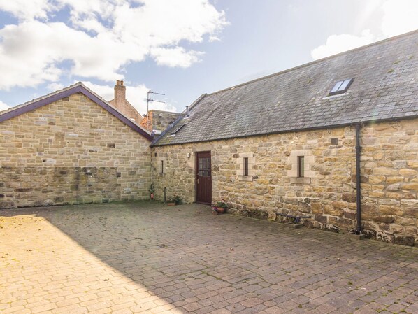A stone building with a tiled courtyard, a wooden door, and a chimney.