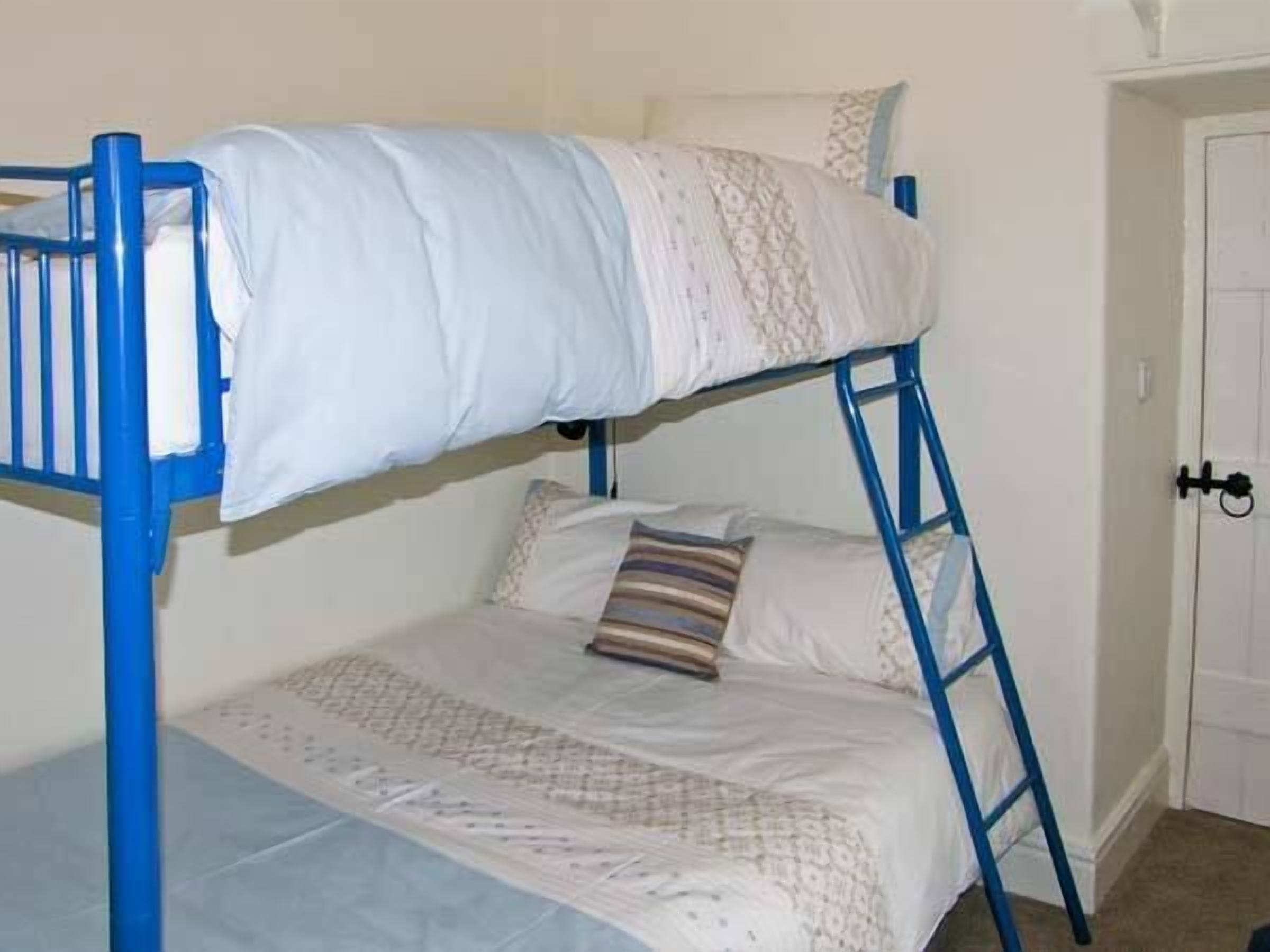 A bunk bed with a blue frame, white bedding, and a patterned pillow.