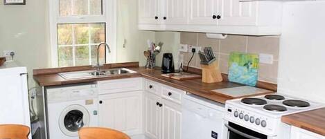 A compact kitchen with white cabinets, a wooden countertop, a sink, a stove, and a washing machine.