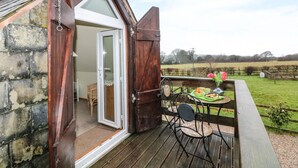 A cozy cottage with a wooden exterior, a glass door leading inside, and a small patio with a table and chairs. - Higher Kernick Stable (Bodmin)