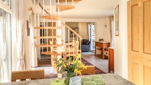A staircase with wooden railings leading to a living area with a sofa, a table, and a vase with flowers. - Higher Kernick Stable (Bodmin)