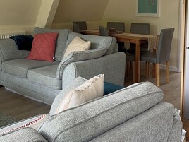 A living room with a grey sofa, a dining table, and chairs.