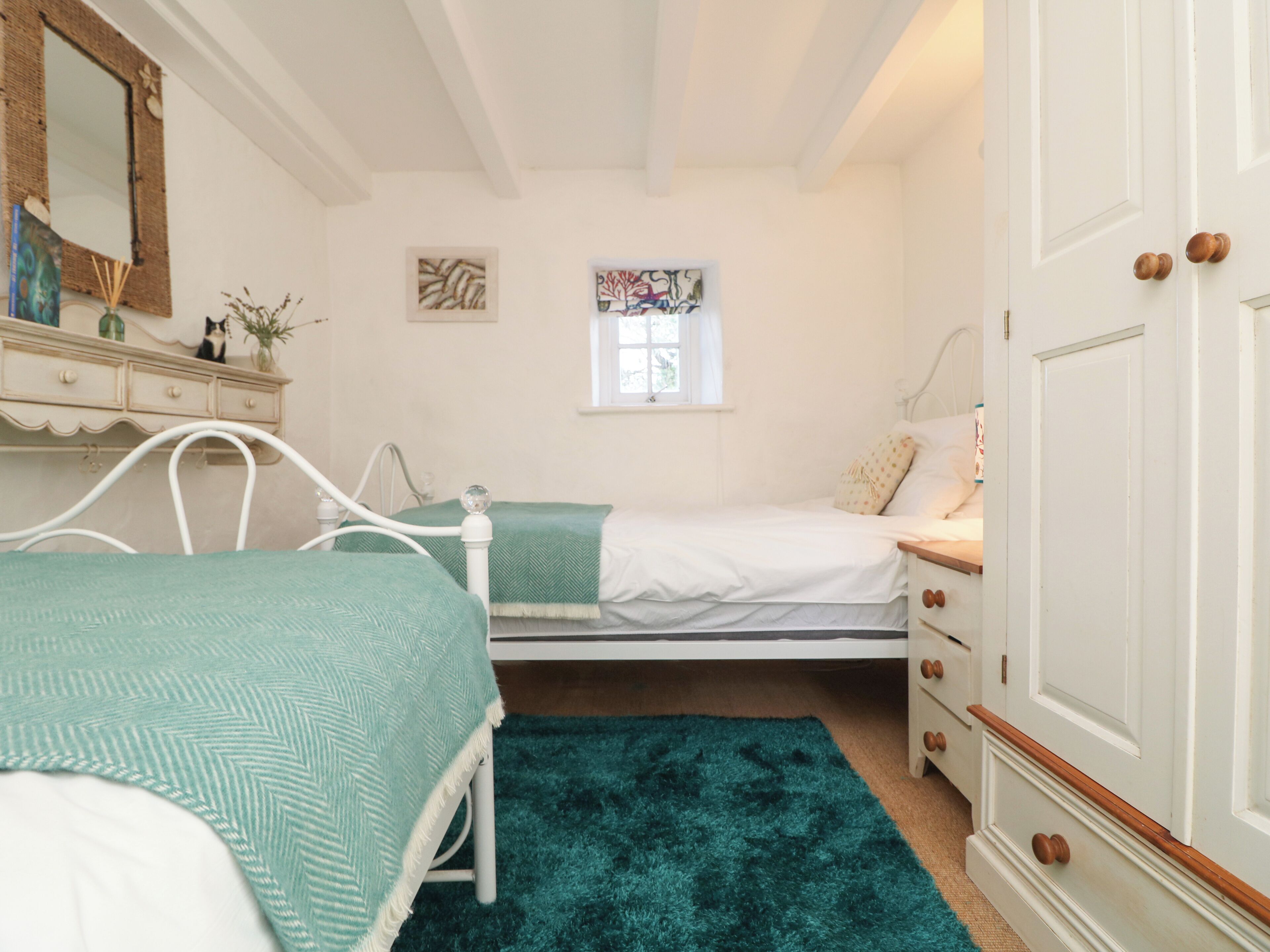 A bedroom with two beds, a dresser, a mirror, and artwork on the walls.