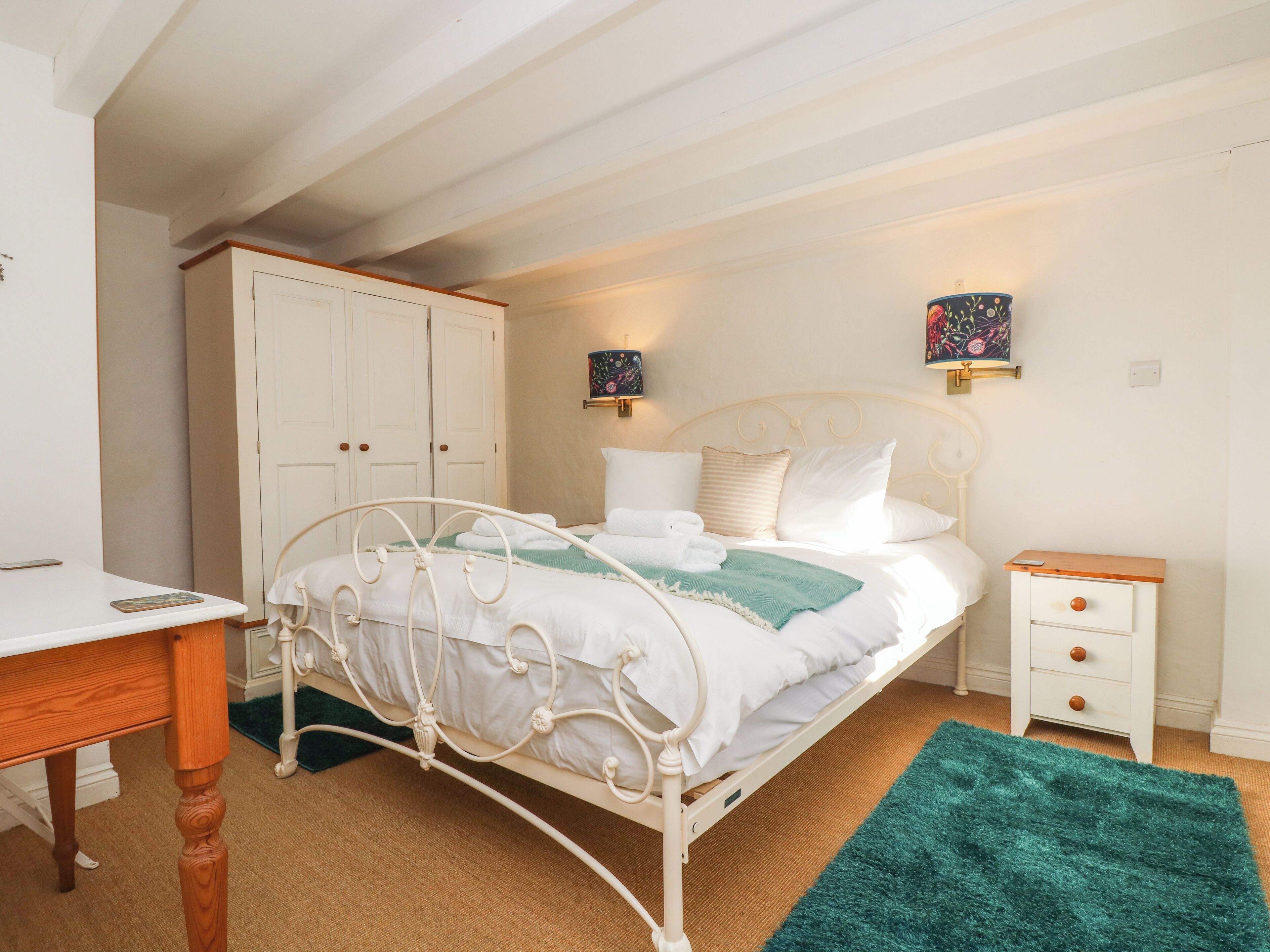A bedroom with a white metal bed frame, a green rug, a bedside table, a nightstand, and a wardrobe.