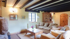A cozy living room with a fireplace, wooden furniture, and a rustic barn door. - Old Winery Cottage (Fowey)