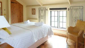 A bedroom with a large bed, a wicker chair, and a window with a view. - Old Winery Cottage (Fowey)