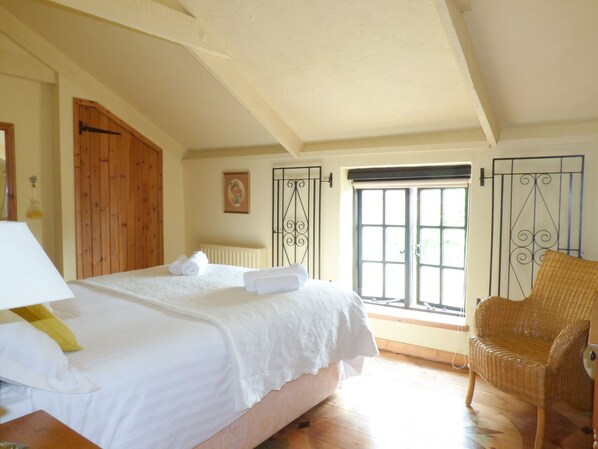 Un dormitorio con una cama grande, una silla de mimbre y un ventanal con vistas.