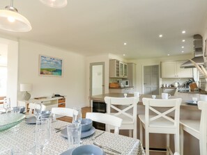 Une cuisine moderne avec des meubles blancs, un coin repas avec une table dressée pour quatre personnes, et une vue sur le salon.