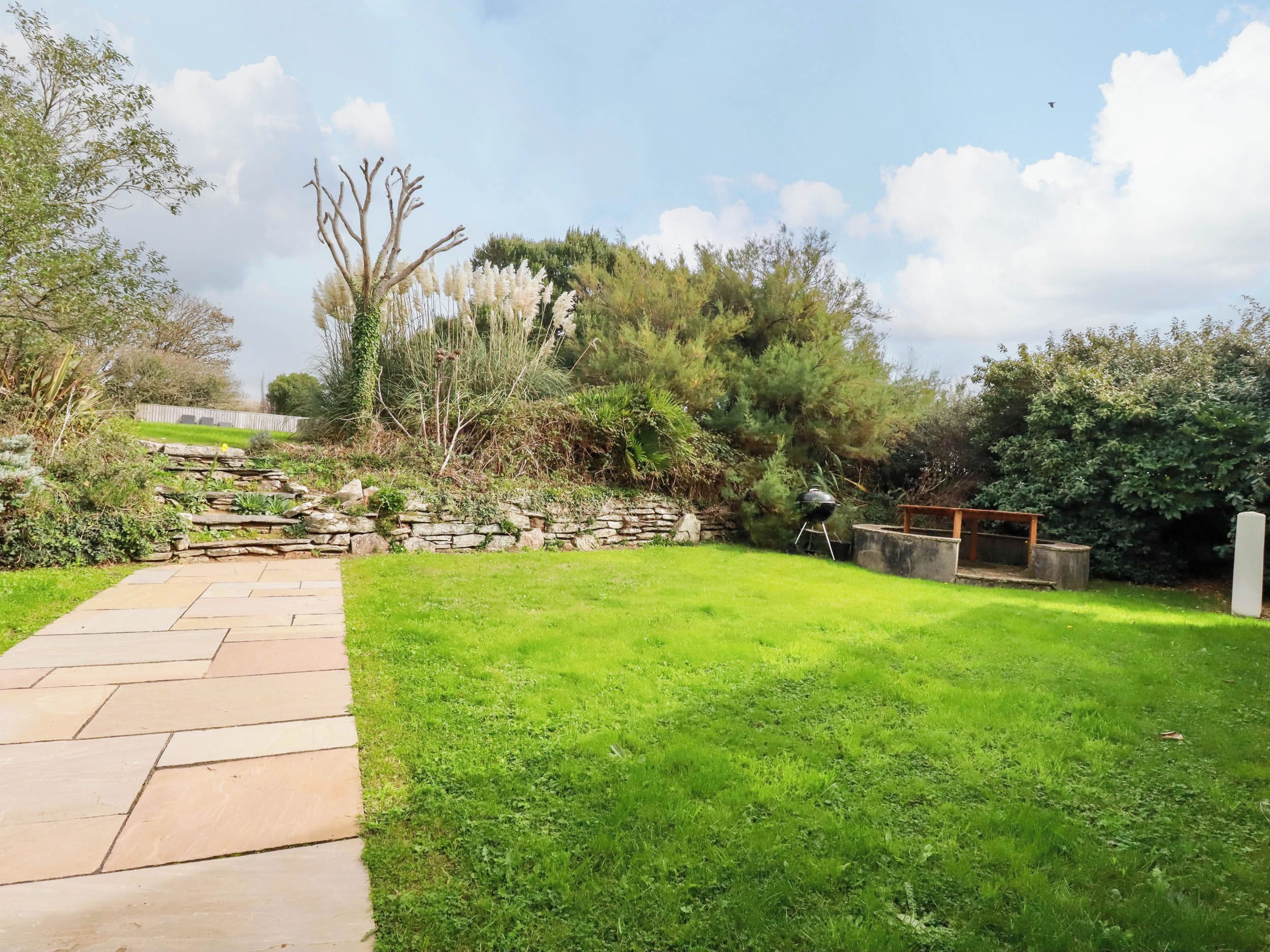 A stone pathway leading through a well-maintained grassy area with a barbecue setup and a stone wall.
