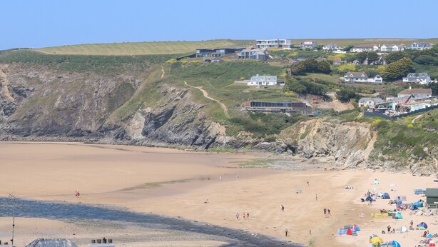 Una zona costera con una playa arenosa, un acantilado rocoso y varias casas en una ladera.