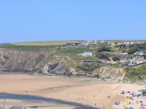 Une zone côtière comprenant une plage de sable, une falaise rocheuse et plusieurs maisons situées sur une colline.