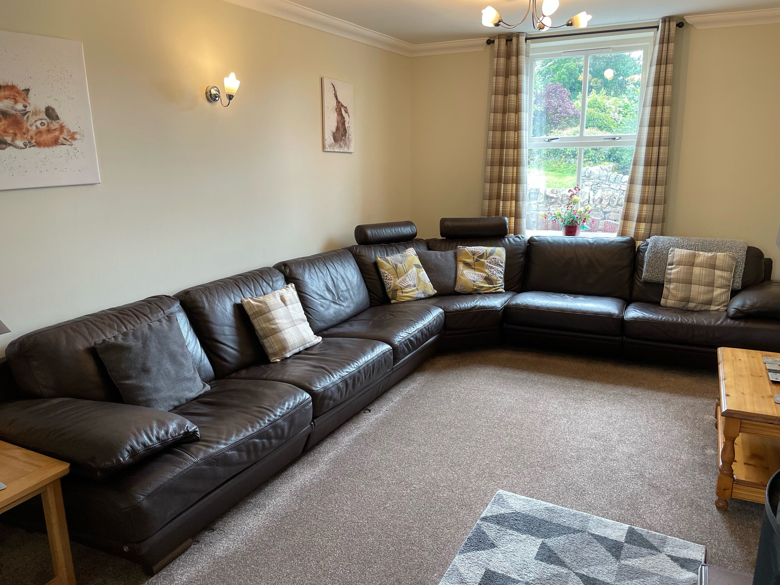 A living room with a large L-shaped dark brown leather sofa, a wooden coffee table, and a patterned rug.