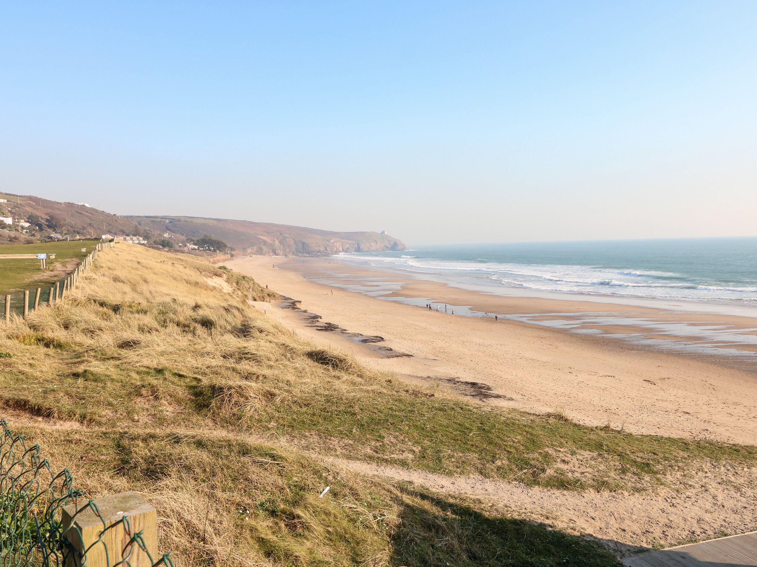 A coastal landscape with a sandy beach, grassy areas, and a wooden fence.