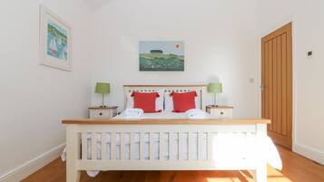 A bedroom with a wooden bed, white bedding, two nightstands with lamps, and two paintings on the wall.