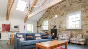Una sala de estar acogedora con una pared de piedra, una chimenea, un sofá y sillones a rayas.