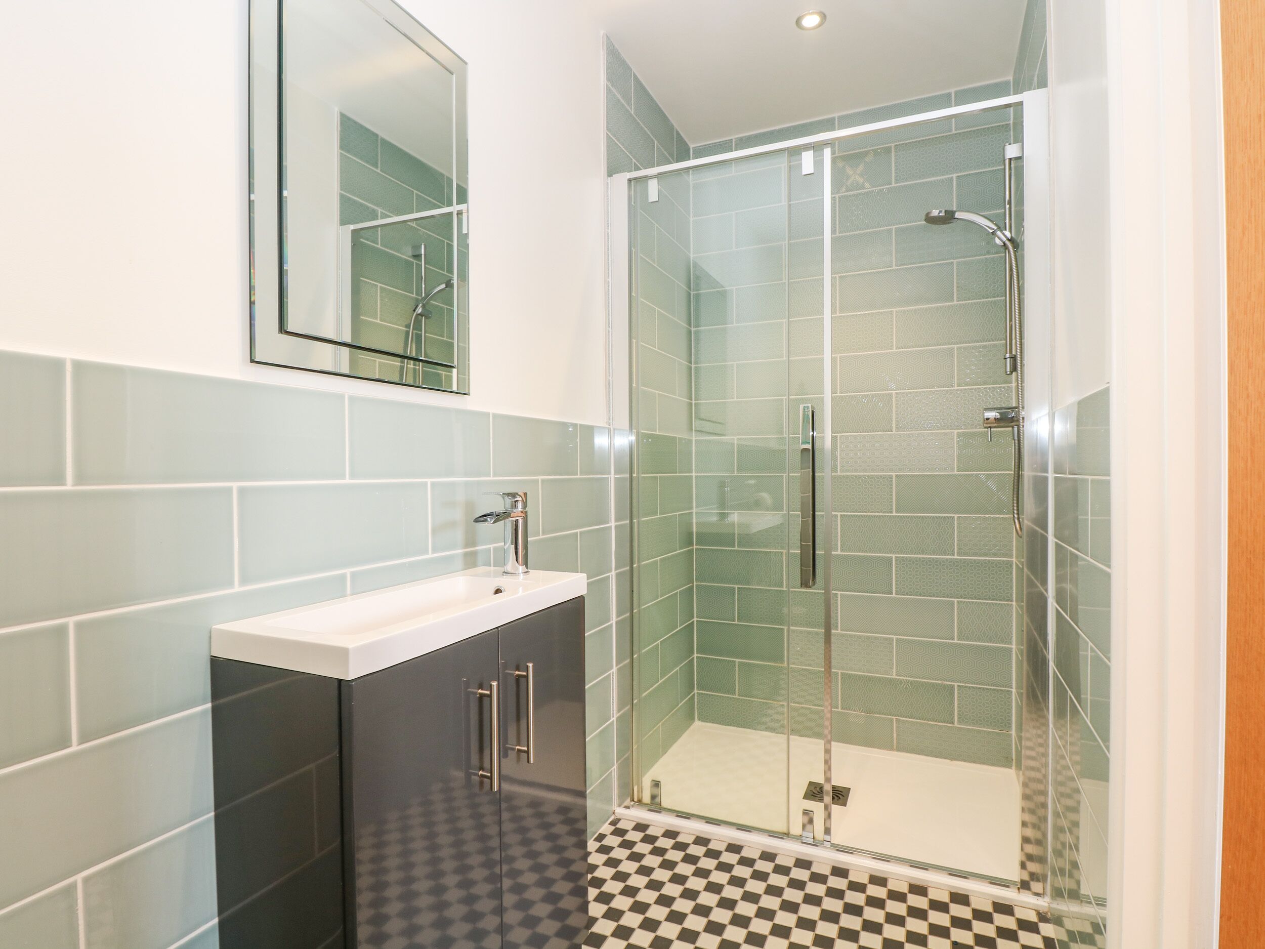 Un baño moderno con ducha envuelta en vidrio, un lavamanos blanco y piso a cuadros.