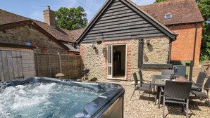 A hot tub in a backyard with a stone building, outdoor seating, and a wooden fence. - The Wain House (Craven Arms)