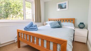 Un dormitorio con una cama de madera, una mesita de noche, un ventanal con cortinas y un cuadro enmarcado en la pared.