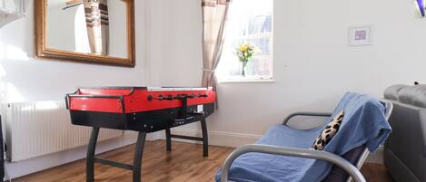 A room with a bed, a red and black table, a window with curtains, a radiator, and a mirror on the wall.