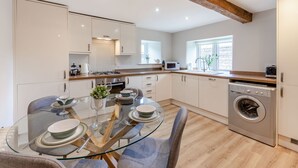Une cuisine moderne avec une table à manger en verre, des poutres en bois et des appareils électroménagers intégrés.