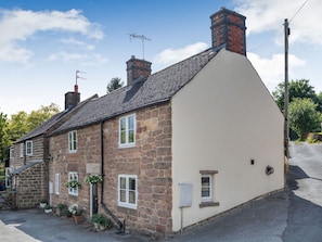 Charming two-story house with a sloped roof, featuring a combination of stone and plaster exteriors, multiple windows, and a chimney.