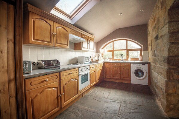 A kitchen with wooden cabinets, a built-in oven, a washing machine, and a skylight. - The Arches (York)