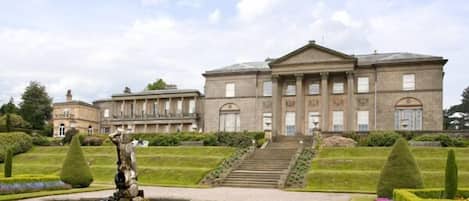 A large, stately building with a formal entrance, a central fountain, and well-manicured gardens.