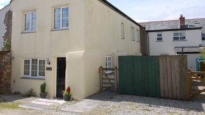 A two-story building with a beige exterior, a small front garden, and a wooden gate. - The Barn (Camelford)