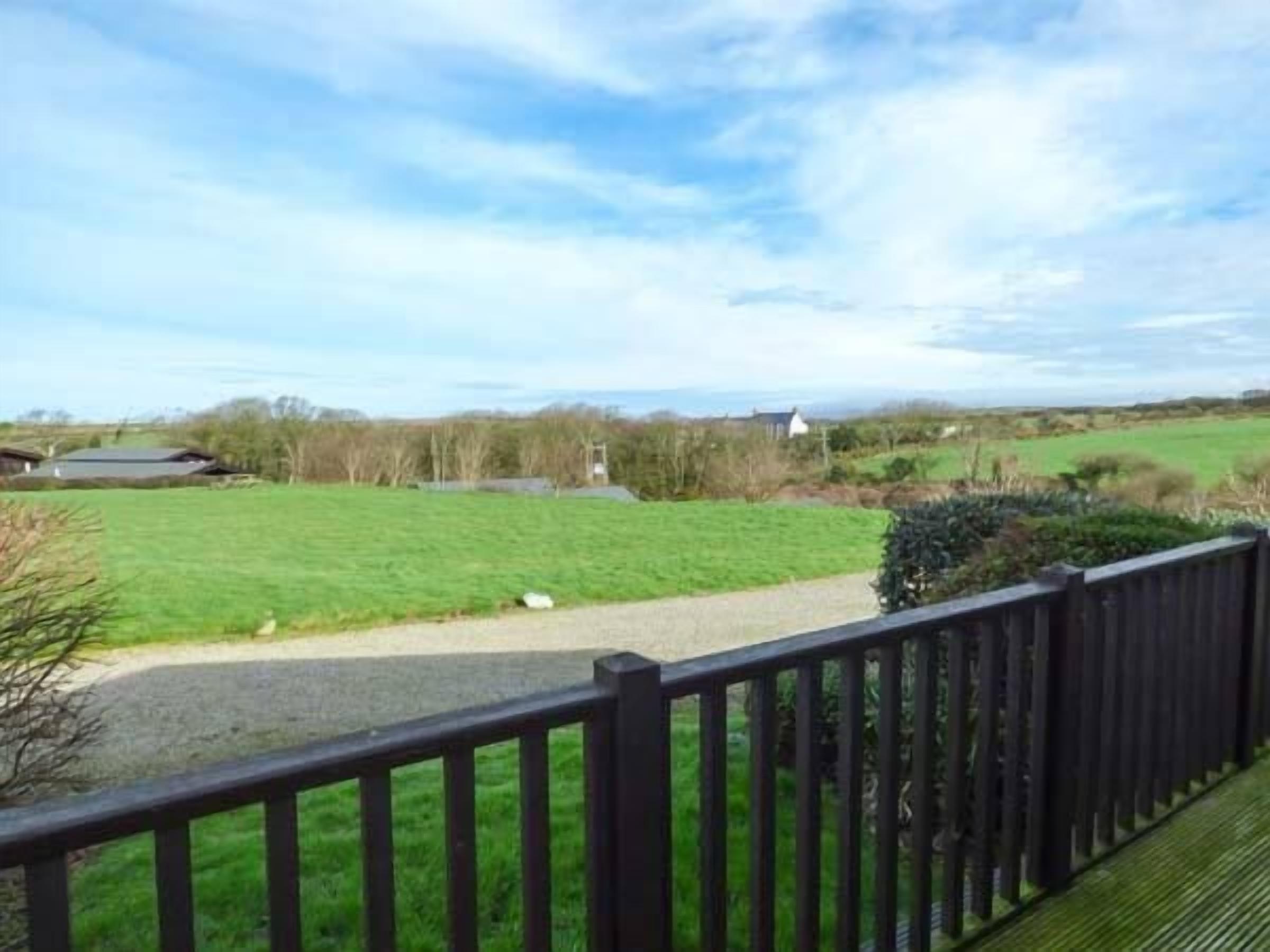 Uitzicht vanaf een balkon met houten hekwerk, op een groen veld en enkele gebouwen in de verte.