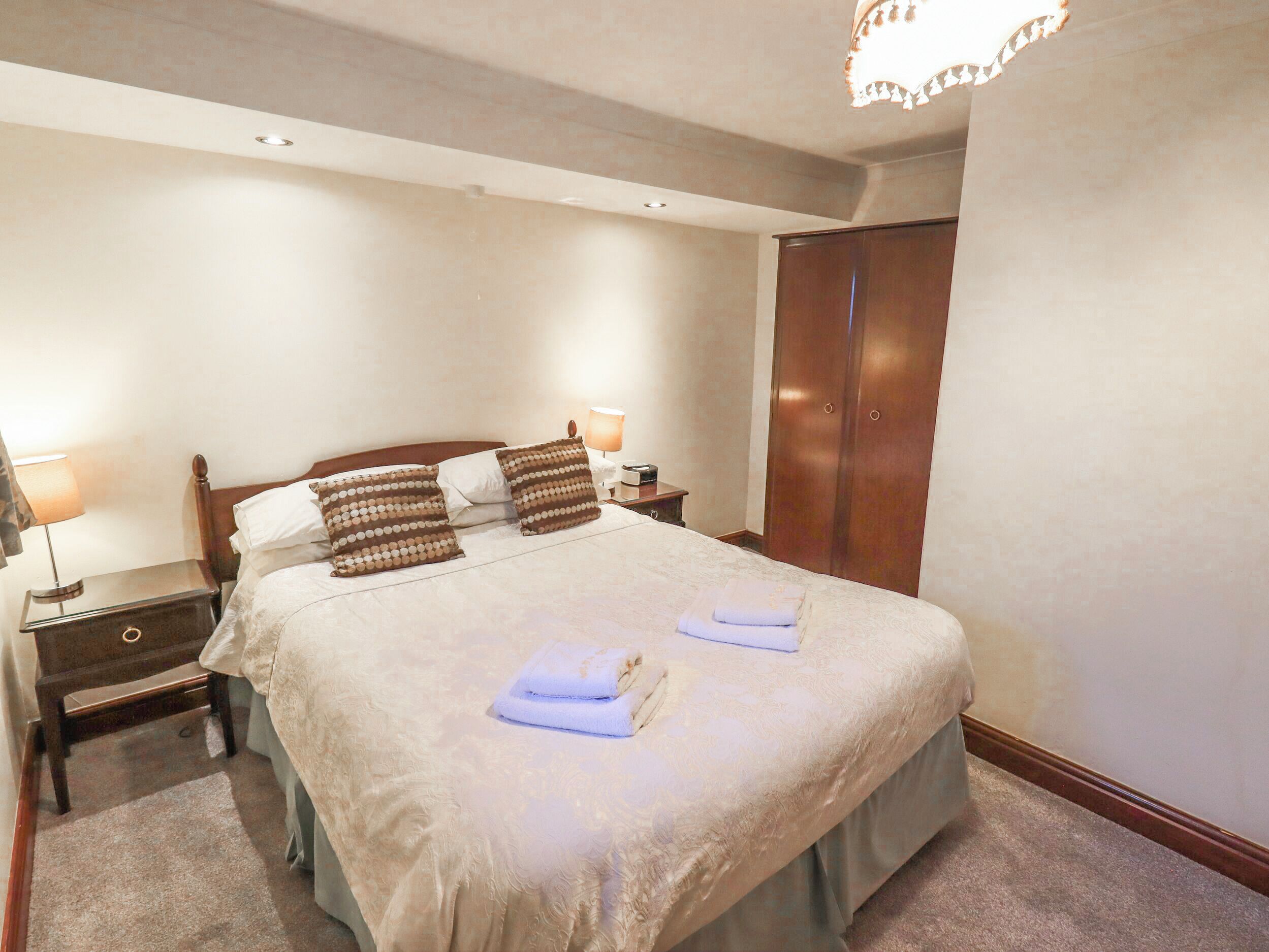 A neatly made bed with pillows, a nightstand with a lamp, and a wooden wardrobe in a hotel room.