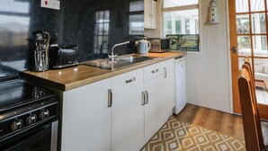 Cozinha com painel de fundo preto, teto de madeira e armários brancos. Há um fogão, micro-ondas e pia. Um tapete estampado está no chão.
