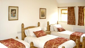 A room with four wooden beds, each with white linens and red floral bedspreads. There are two framed pictures on the walls, and a window with curtains. - Happy Union Stables (Llandrindod Wells)