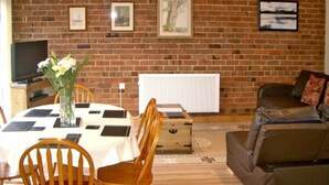 A dining area with a brick wall, a white table, wooden chairs, and a brown sofa. - Happy Union Stables (Llandrindod Wells)