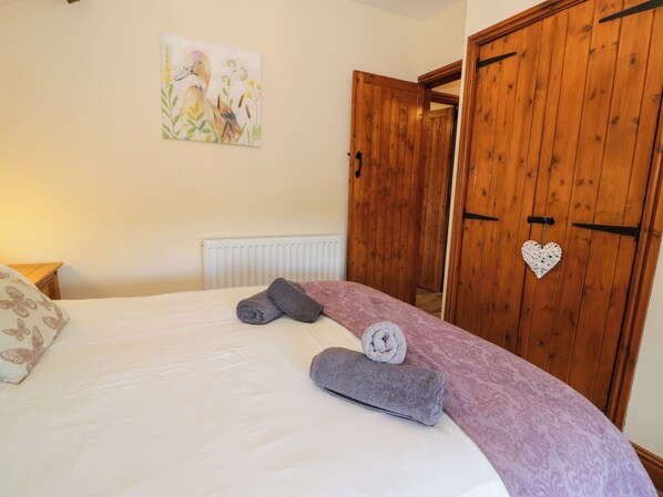 A bedroom with a bed, a radiator, wooden wardrobe doors, and a wall painting. - Cornel Clyd (Abergele)