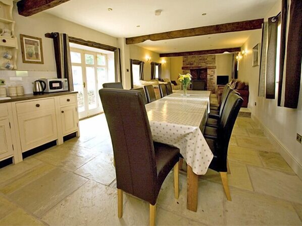 A dining area with a long table, chairs, and a kitchen area with cabinets and appliances.