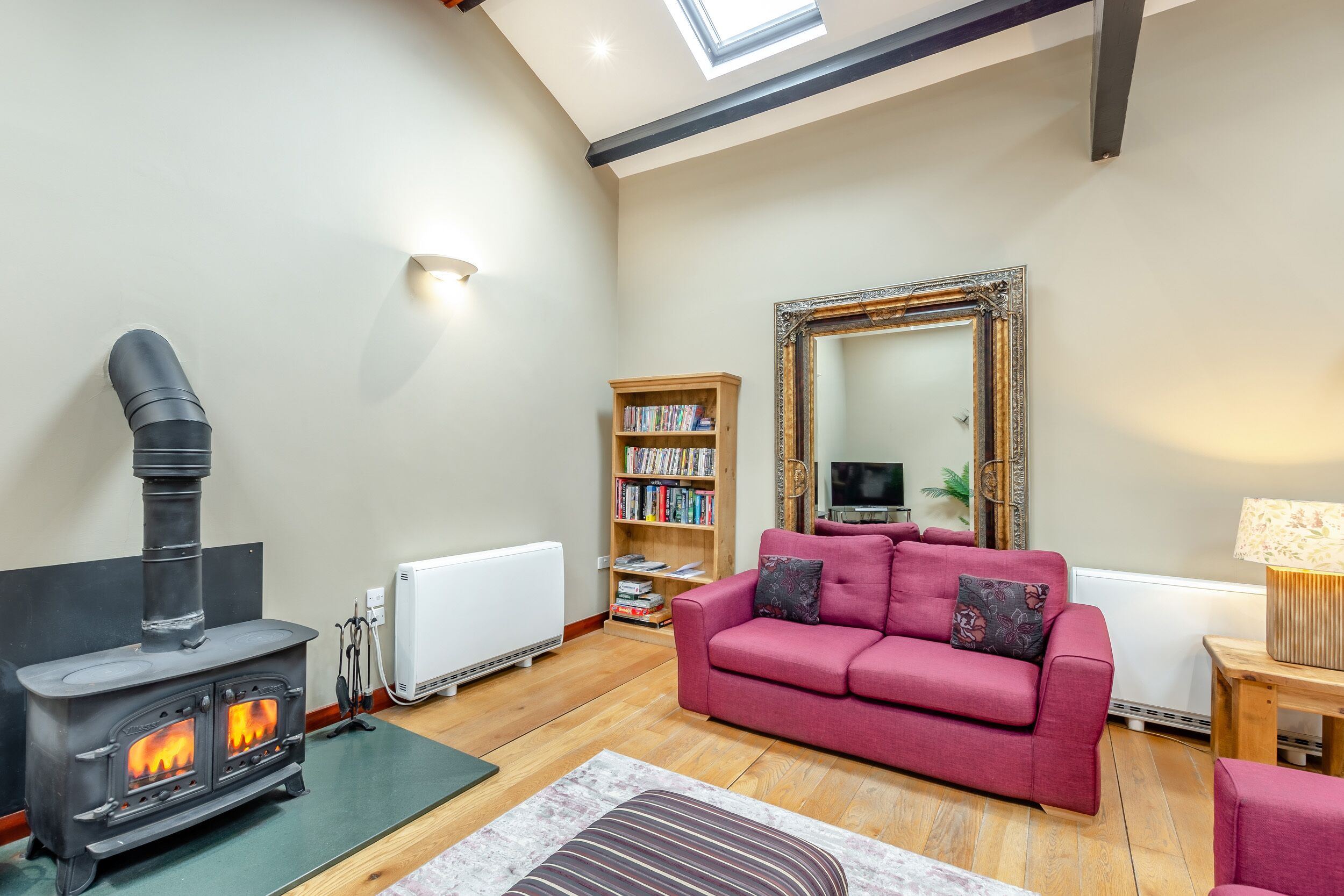 A cozy living room with a wood-burning stove, a red sofa, a bookshelf, and a large mirror.