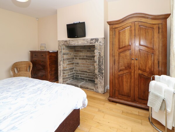 Een slaapkamer met een bed, een houten garderobe, een stenen openhaard en een televisie aan de muur.